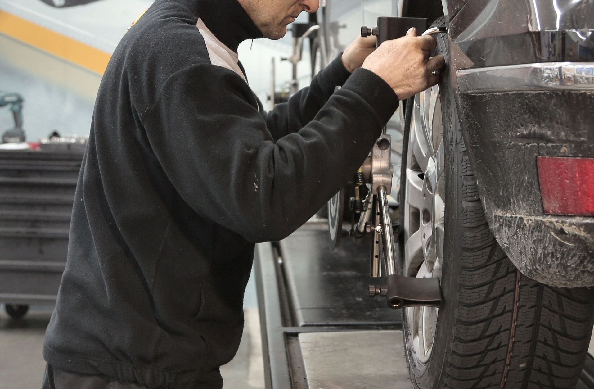 Side view of a mechanic aligning a car tire in a professional auto workshop.
